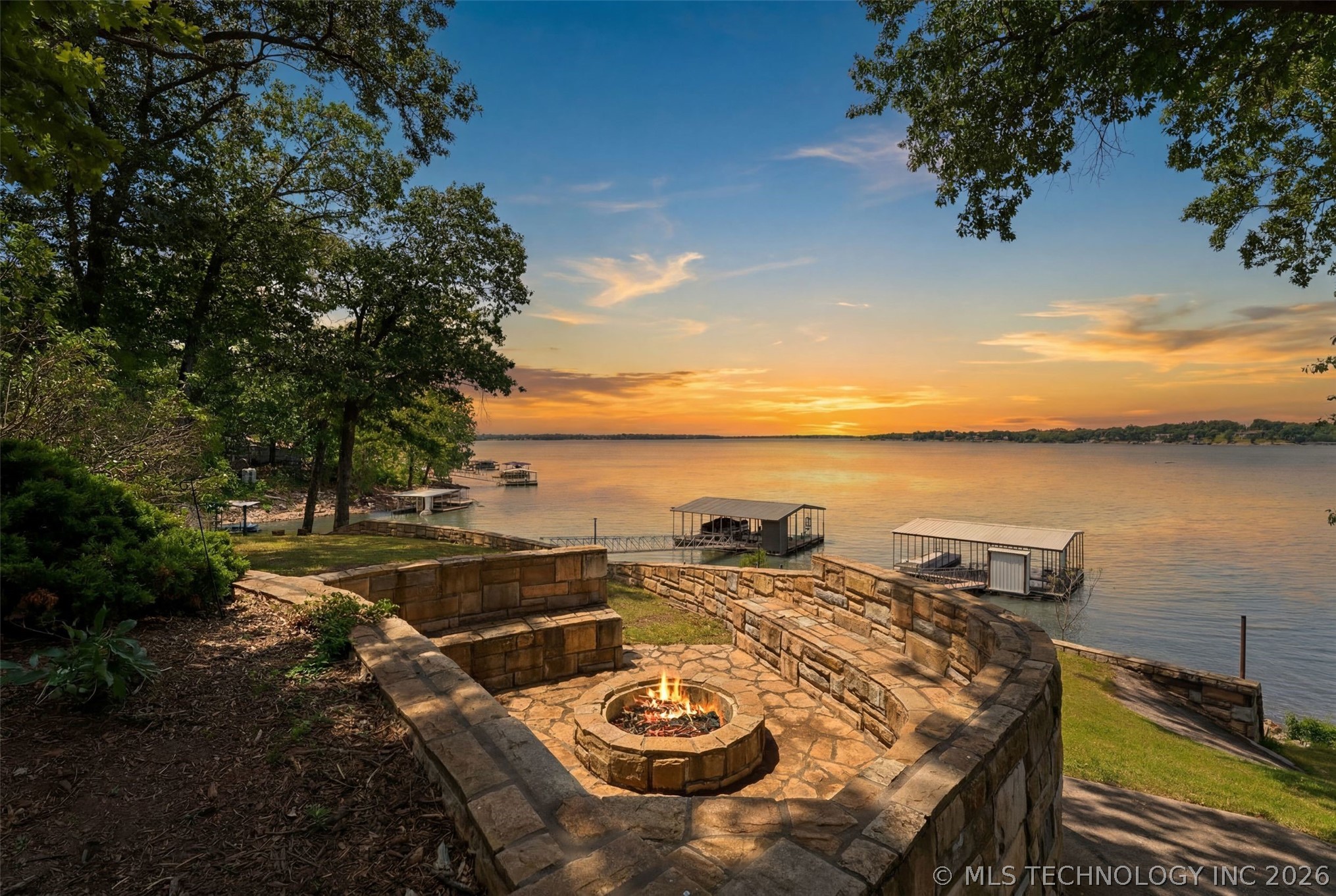 Stone fire pit overlooking Grand Lake at sunset, with the private dock visible on the right and the sky in deep orange and indigo