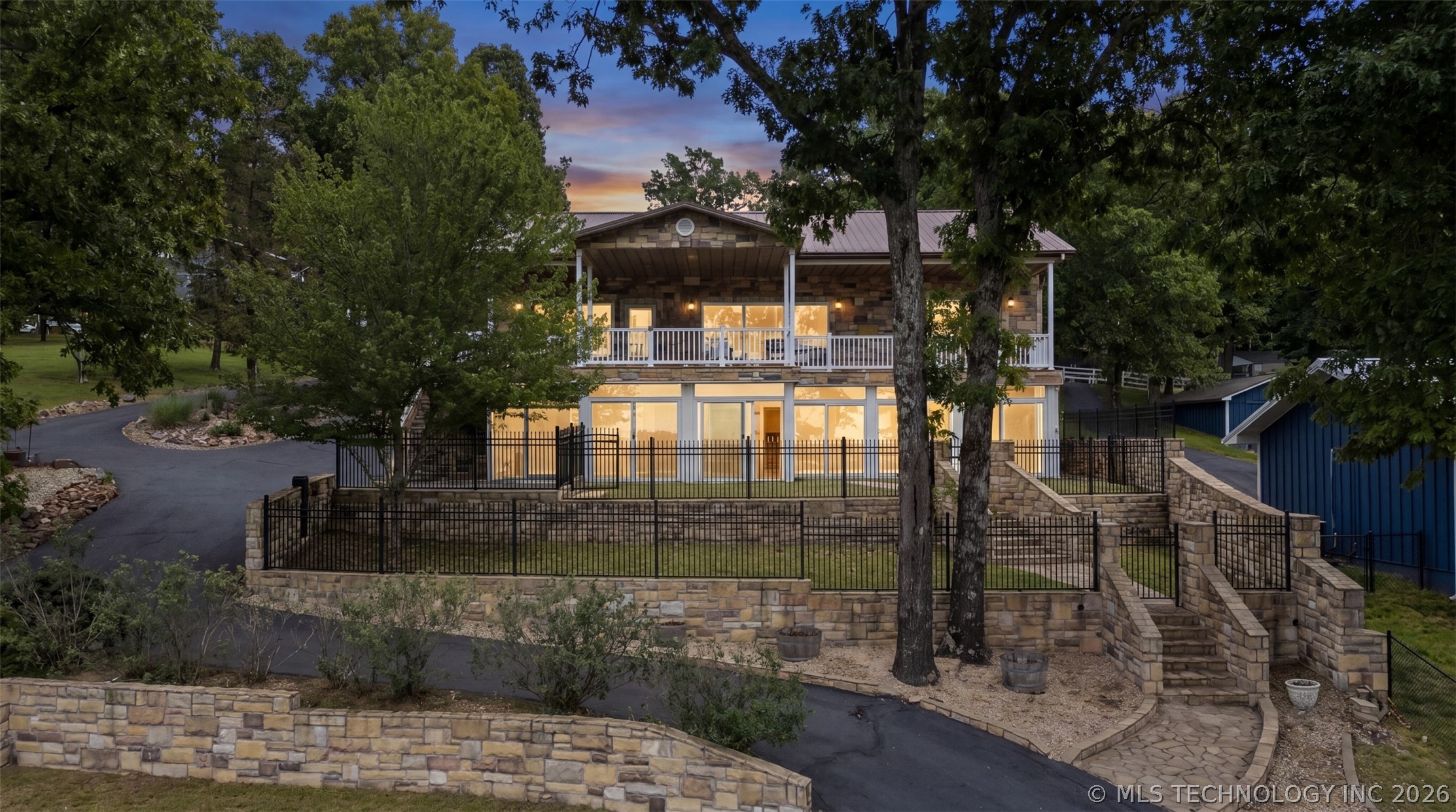 Front elevation of the residence at twilight, the upper deck and great-room windows lit warm against a pink sky
