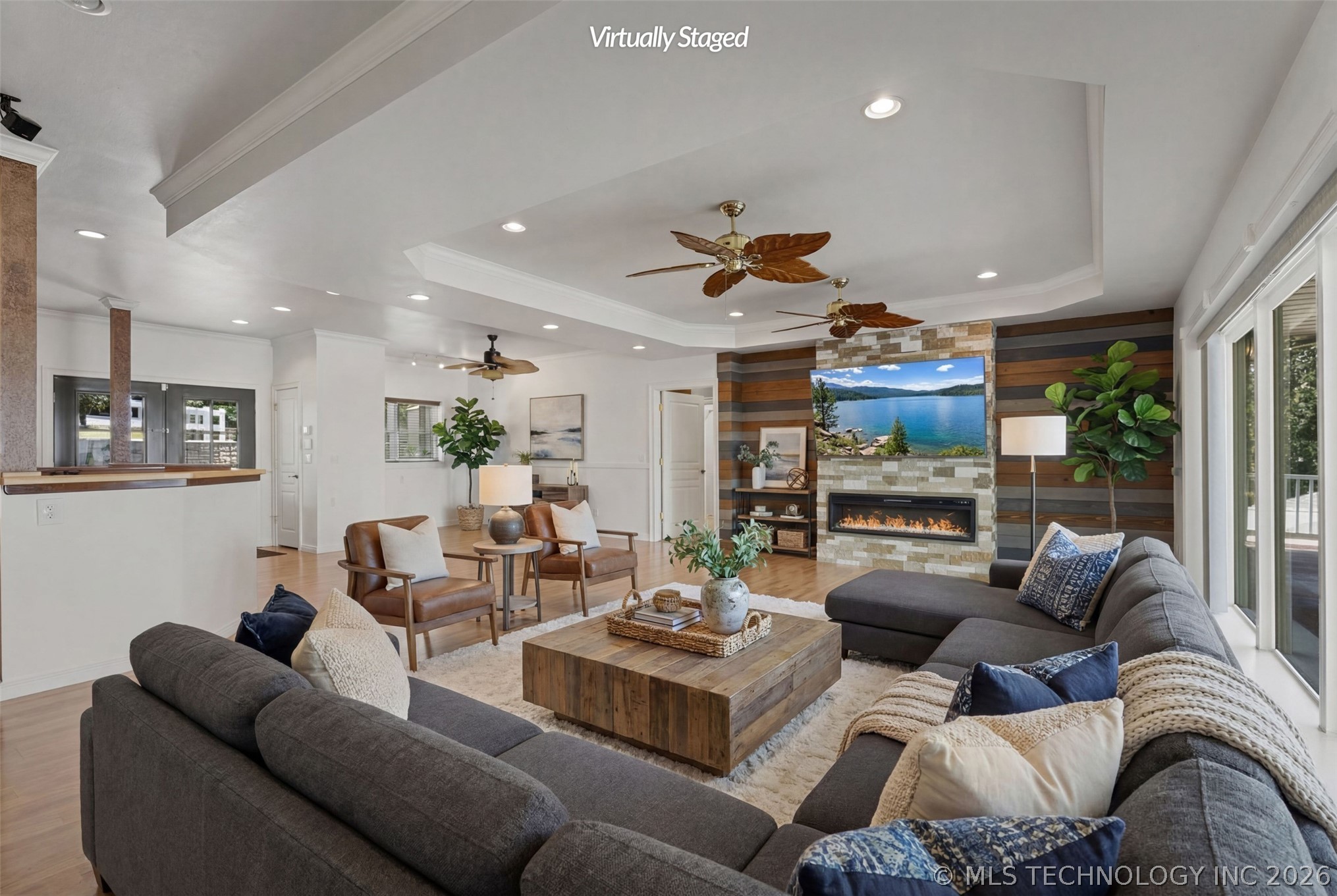 Great room with reclaimed-wood feature wall, stacked-stone fireplace surround, and a tray ceiling looking out to the lake through sliding doors