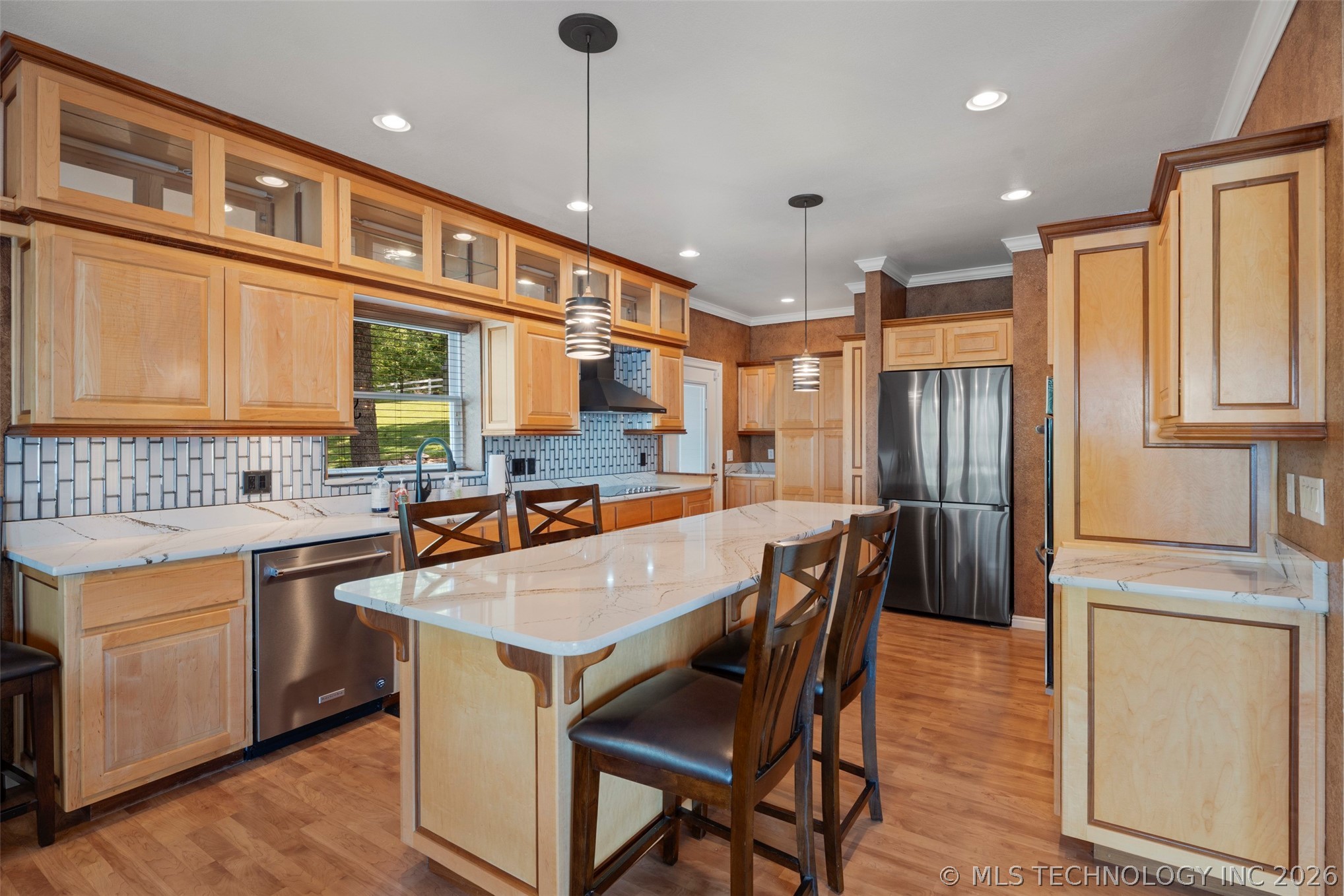 Kitchen with maple cabinetry, marbled granite-and-stone counters, glass-tile backsplash, and a generous island with seating for four