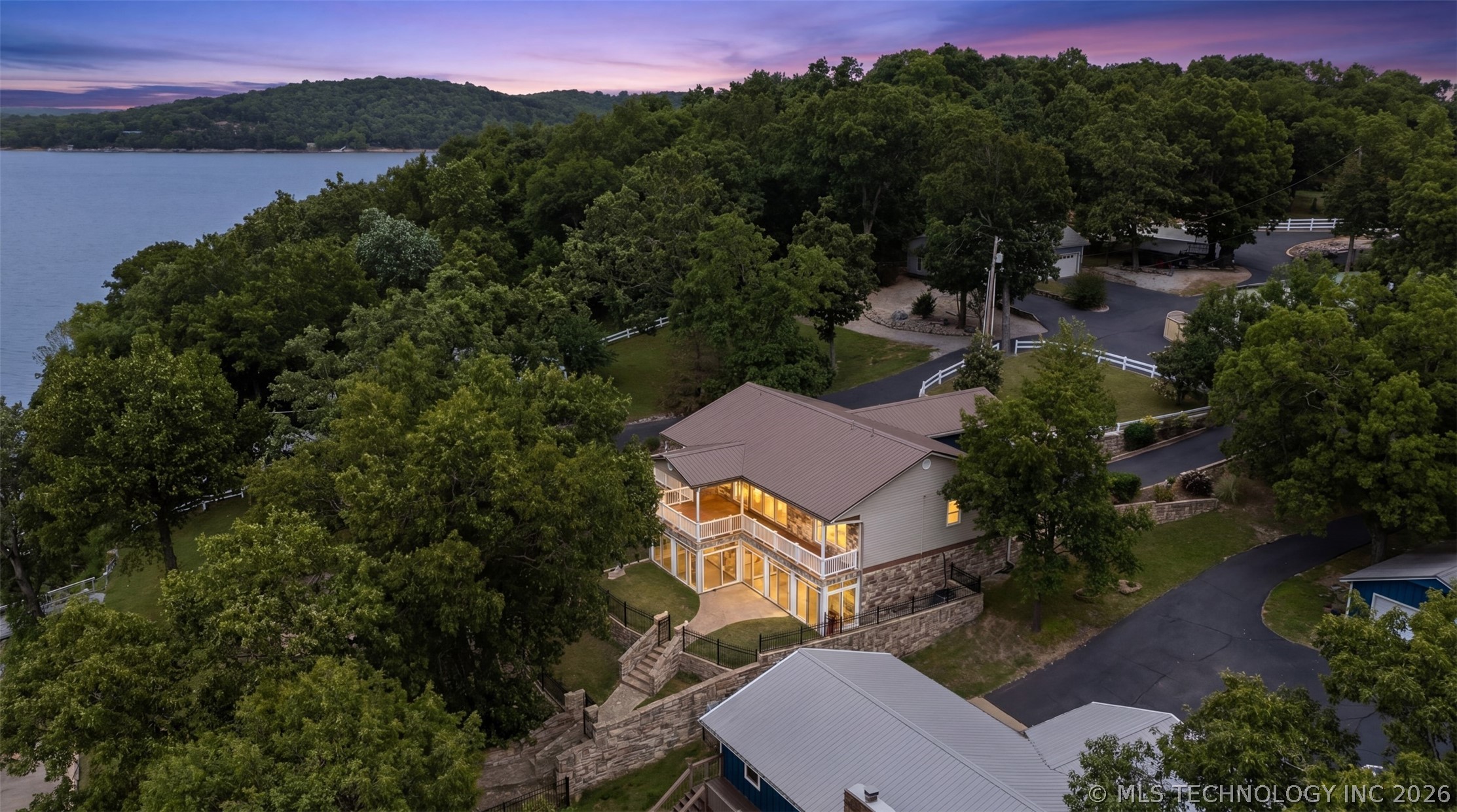 Aerial twilight view of the residence on its gated lot, with mature oaks framing the property and Grand Lake on the west